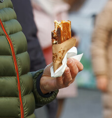 A close-up of a person holding a freshly grilled sandwich wrapped in paper at Naplavka outdoor farmers market in Prague.