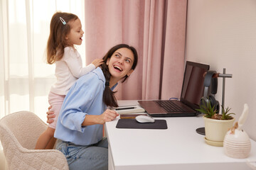 Happy mother working from home laughing while child plays and distracts her