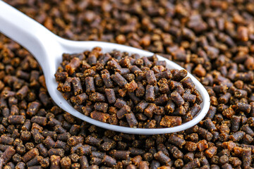 Dry food for aquarium fish on  spoon compound fish feed flakes.Pile of flakes and granules for feeding tropical aquarium fishTop view.Aquarium