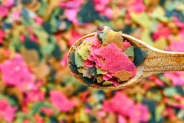 Dry food for aquarium fish on a wooden spoon compound fish feed flakes.Pile of flakes and granules...