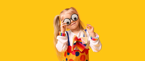 Funny little girl in clown costume with glasses on yellow background