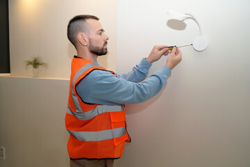 Man is focused on installing a wall light fixture in his home. He is wearing a safety vest and using a screwdriver to complete the repair task in just one hour