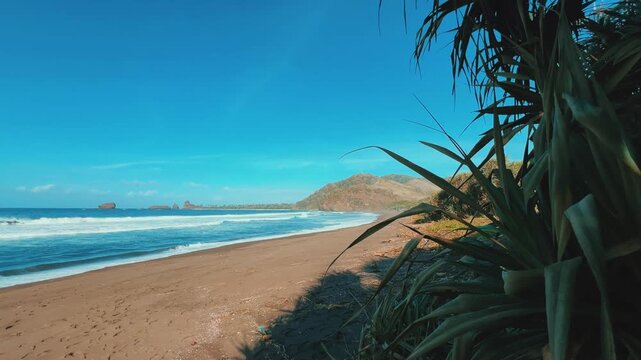 The sea in Jember, East Java. Indonesia. Watu Ulo beach with dark sand, mountains and coral rocks towering above the beach. The raging blue Indian ocean on a sunny day. 4К