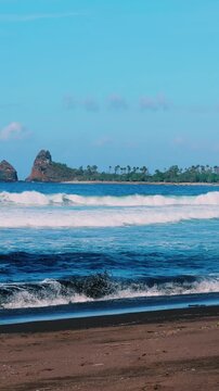 The sea in Jember, East Java. Indonesia. Watu Ulo beach with dark sand, mountains and coral rocks towering above the beach. The raging blue Indian ocean on a sunny day. 4К