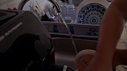View of a person's hands diligently scrubbing a small pot under a stream of running water in a modern kitchen sink. It captures the essence of everyday domestic tasks and maintaining a clean home.