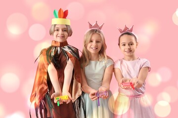 Cute kids in festive costumes with and graggers on pink background. Purim celebration