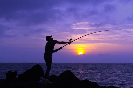 Dramatic Purple Sunset Behind an Arched Fisherman Silhouette
A single fisherman's silhouette is captured mid-cast on the rocky shore, his rod dramatically arched against a vibrant purple and orange  - Powered by Adobe