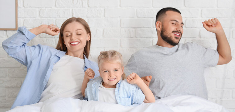 Cute little girl and her parents with soft blanket waking up in bedroom - Powered by Adobe