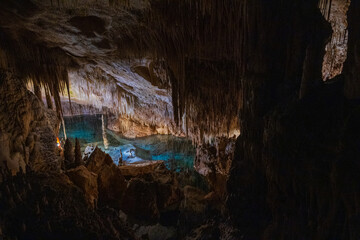 Mystical underground cave illuminated by soft artificial light, showcasing dramatic stalactites, rock formations, and reflections over a still subterranean lake