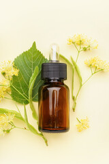 Bottle of essential oil and fresh linden flowers on color background