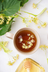 Cup of linden tea and bowl with honey on white table
