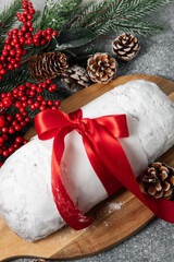 christmas stollen holiday dessert with red ribbon and pine decorations on wooden board