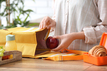 Woman packing fresh meal into lunch box bag in kitchen