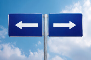 Two adjacent blue road signs with white arrows pointing in opposite directions—left and right—symbolizing decision-making, choices, or diverging paths against a bright sky backdrop