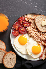 Plate of tasty English breakfast with fried eggs on black background