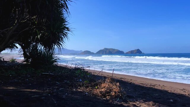 The sea in Jember, East Java. Indonesia. Watu Ulo beach with dark sand, mountains and coral rocks towering above the beach. The raging blue Indian ocean on a sunny day. 4К