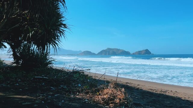 The sea in Jember, East Java. Indonesia. Watu Ulo beach with dark sand, mountains and coral rocks towering above the beach. The raging blue Indian ocean on a sunny day. 4К	