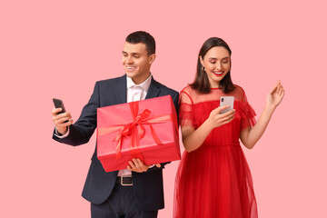 Young couple with mobile phones and gift box on pink background. Online dating