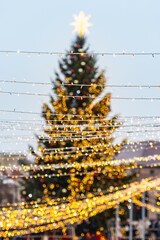 A large outdoor Christmas tree in Vilnius, decorated with warm white lights and ornaments, topped with a glowing star, standing in a festive setting with strings of lights in the foreground