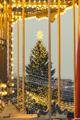A large outdoor Christmas tree in Vilnius, decorated with warm white lights and ornaments, topped with a glowing star, standing in a festive setting with strings of lights in the foreground
