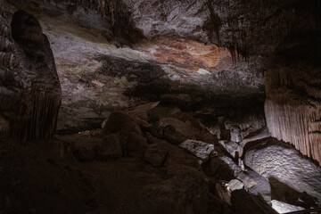 Large underground chamber filled with dense stalactites and rock formations, illuminated by soft artificial light inside a deep limestone cave