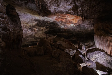 Large underground chamber filled with dense stalactites and rock formations, illuminated by soft artificial light inside a deep limestone cave