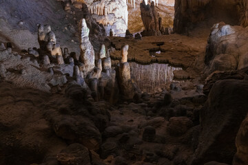 Large underground chamber filled with dense stalactites and rock formations, illuminated by soft artificial light inside a deep limestone cave