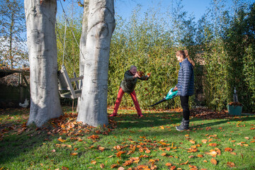 Family members enjoy autumn gardening, a friend happily throws a pile of colorful leaves up into the air from a leaf blower while cleaning the garden.