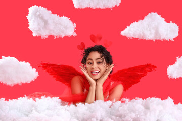 Fototapeta premium Young African-American woman dressed as Cupid in clouds on red background. Valentine's Day celebration