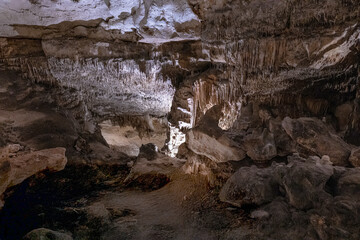 Large underground chamber filled with dense stalactites and rock formations, illuminated by soft artificial light inside a deep limestone cave