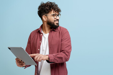 Smiling man with curly hair and beard using a tablet on a light blue background