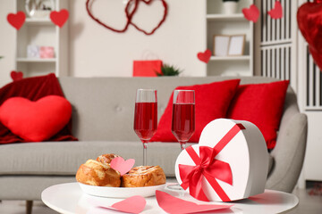 Heart-shaped gift box, glasses of wine and sweet buns on coffee table in living room. Valentine's Day celebration
