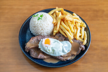 Delicious bitoque de vaca served with fried potatoes and rice, featuring a perfectly cooked egg on top, showcasing a traditional meal presentation
