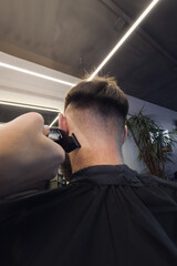 Professional barber wielding electric hair clipper making Fashionable haircut. Bearded Man client visit gentleman grooming beauty salon for hairstyle care. Modern Haircut style in barber shop close up