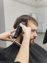 Professional barber wielding electric hair clipper making Fashionable haircut. Bearded Man client visit gentleman grooming beauty salon for hairstyle care. Modern Haircut style in barber shop close up