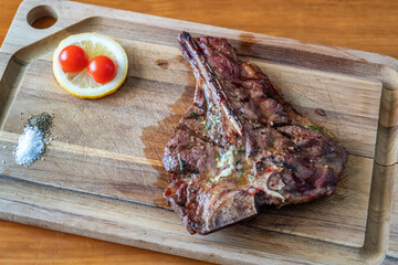T-bone steak grilled to perfection on a wooden cutting board, garnished with lemon and cherry tomatoes, showcasing delicious culinary presentation