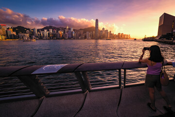 Scenic, awesome view of tourist photographing Victoria Harbour and Hong Kong's fantastic skyline, against a dramatic sunset and sky, Hong Kong, China