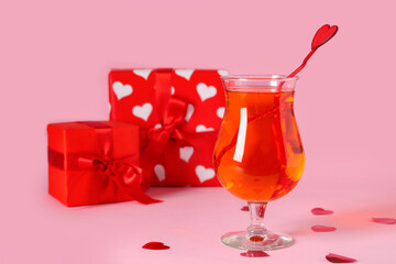 Glass of tasty cocktail with hearts and presents on pink background, closeup. Valentine's Day celebration