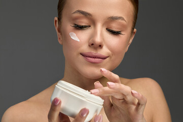 Woman applying moisturizer to her face in a beauty routine at home during the evening, promoting a healthy skincare regimen and self-care practice