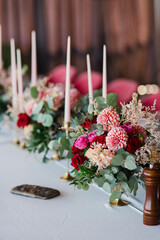 Coziness and style. Modern event design. Table setting at wedding reception. Floral compositions with beautiful flowers and greenery, candles, laying and plates on decorated table.