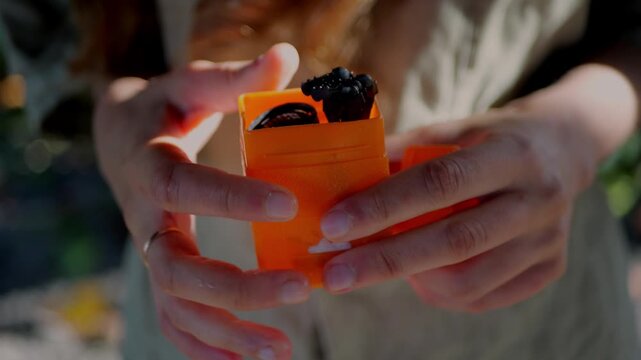Woman removes compact camping stove burner from bright orange case outdoors, demonstrating lightweight backpacking cooking gear and minimalist camp setup.