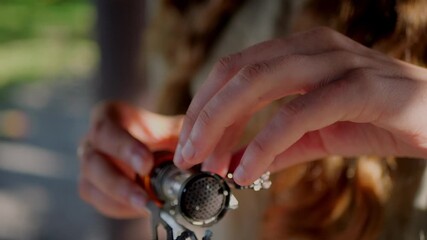 Hands adjust compact camping stove burner, folding tiny pot supports and checking mesh head while preparing lightweight backpacking cooker outdoors.