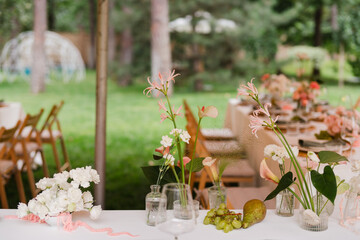 Coziness and style. Modern event design. Table setting at wedding reception. Floral compositions with beautiful flowers and greenery, candles, laying and plates on decorated table.