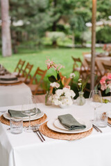 Coziness and style. Modern event design. Table setting at wedding reception. Floral compositions with beautiful flowers and greenery, candles, laying and plates on decorated table.