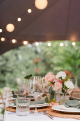 Coziness and style. Modern event design. Table setting at wedding reception. Floral compositions with beautiful flowers and greenery, candles, laying and plates on decorated table.