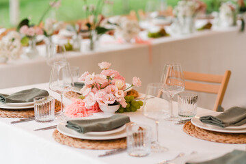Coziness and style. Modern event design. Table setting at wedding reception. Floral compositions with beautiful flowers and greenery, candles, laying and plates on decorated table.