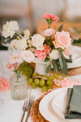 Coziness and style. Modern event design. Table setting at wedding reception. Floral compositions with beautiful flowers and greenery, candles, laying and plates on decorated table.