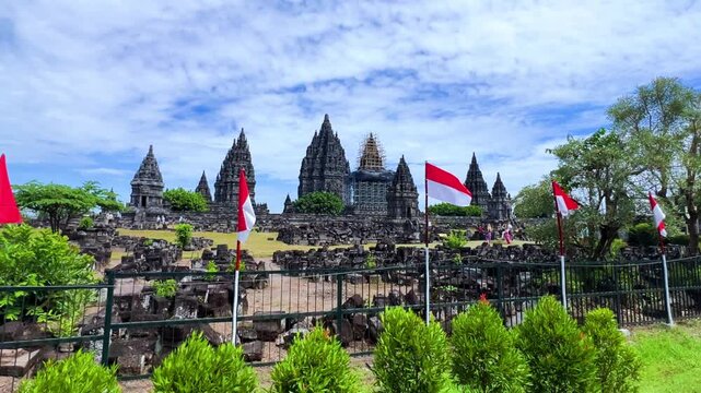 View of the ancient Prambanan Temple, a Hindu temple complex in Yogyakarta, Indonesia. The temple rises above the green foliage under a blue sky. The towers cast shadows on a sunny day. 4К