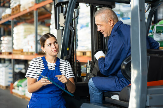 Mature man drive operate automatic fork lift loader and answers young female auditors questions. Girl conducts survey of senior male employee and writes data to report
