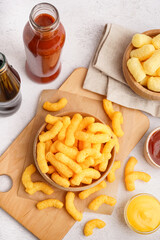 Bowls with different tasty salty corn sticks and sauces on light background